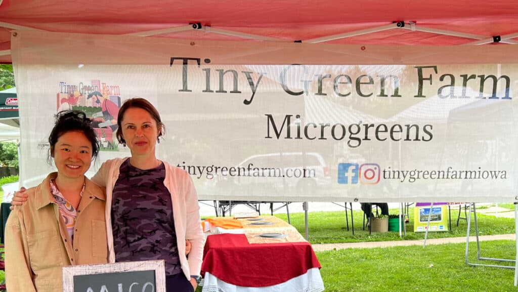 Tiny Green Farm proprietors standing in front of banner at farmer's market booth.
